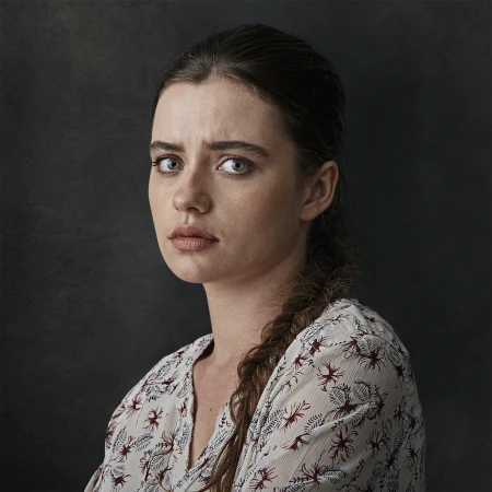 Portrait of a woman with braided hair wearing a patterned white top against a dark mottled background by Michele Aboud