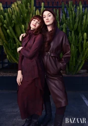 Two women posing together in burgundy outfits in front of a tall green cactus garden outdoors in Sydney.