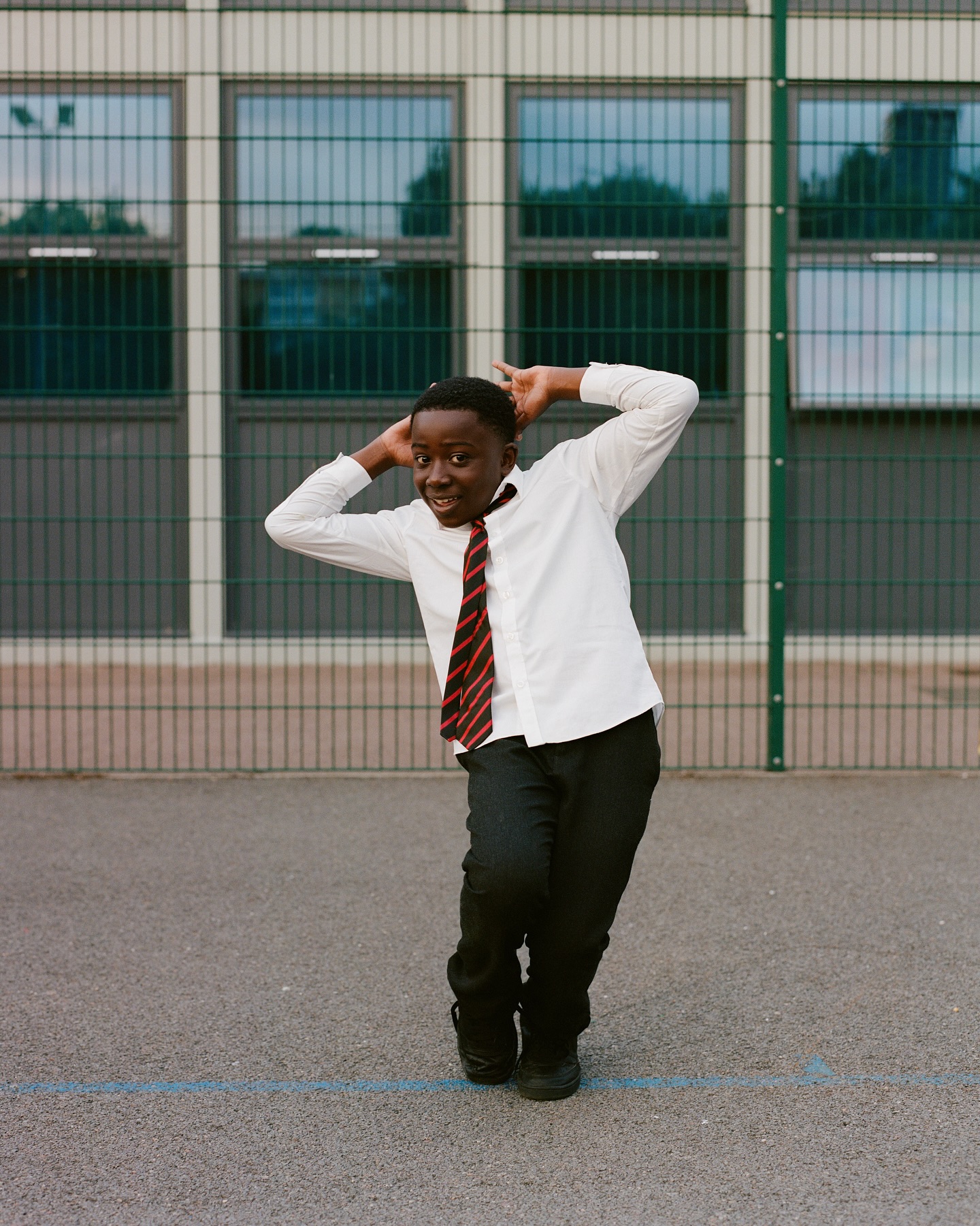 Young boy in school uniform poses playfully against a building, showcasing a candid moment in an urban school setting.