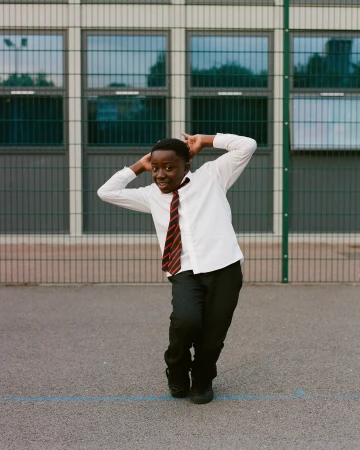 Young boy in school uniform poses playfully against a building, showcasing a candid moment in an urban school setting.