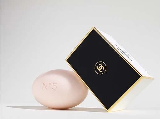 Still life of Chanel No. 5 soap and the associated packaging. The soap is light pink with the number 5 embossed on its surface.