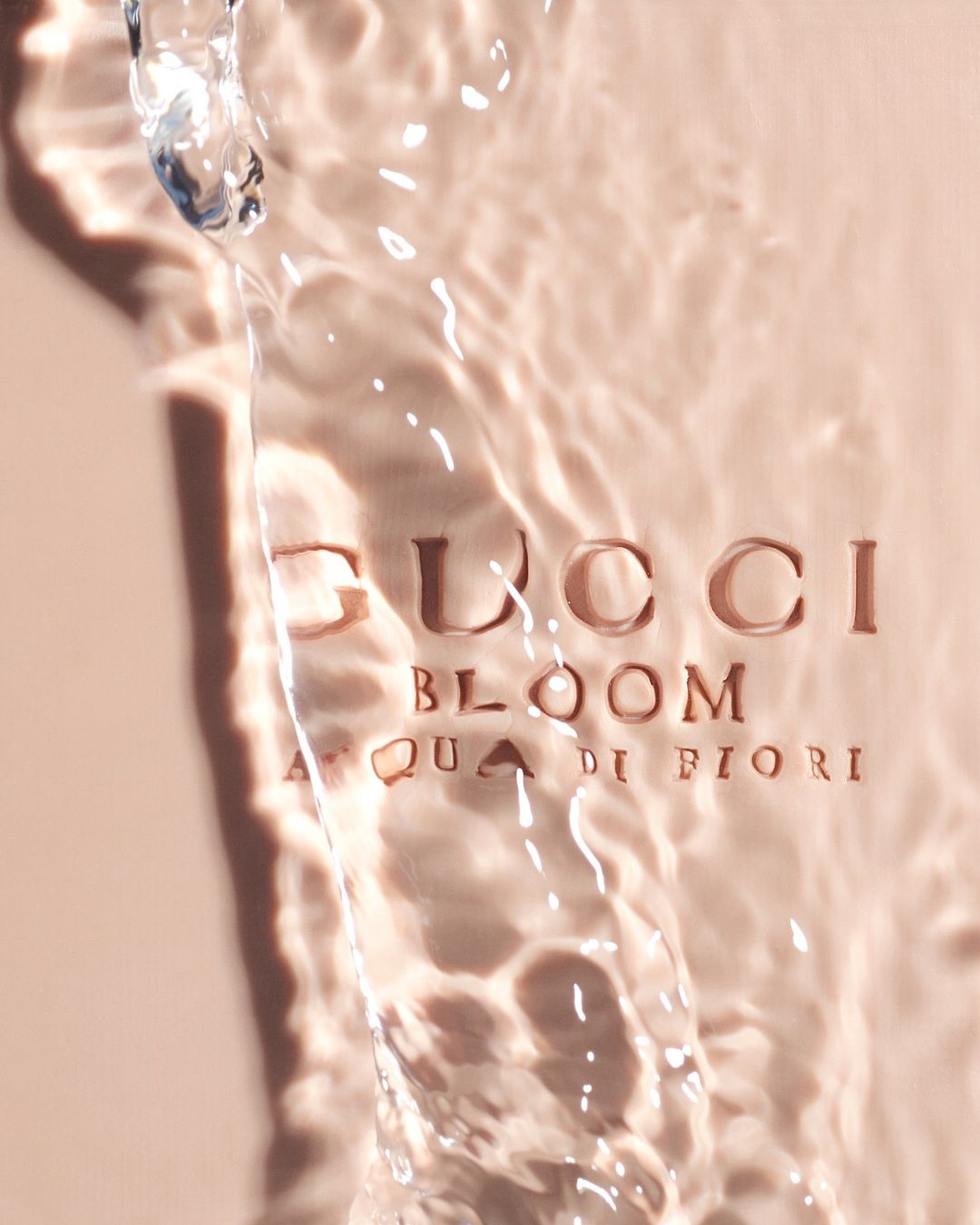 Gucci Bloom Acqua di Fiori perfume bottle with water cascading over the brand logo in a beauty and fashion advertisement.