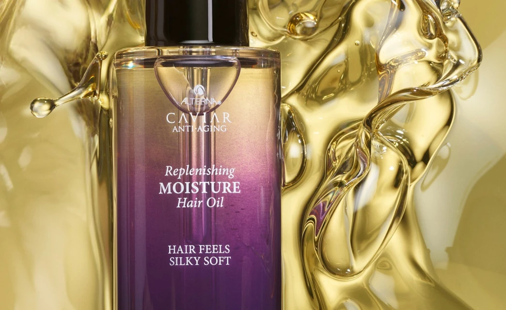 Alterna Caviar Anti-Aging Replenishing Moisture Hair Oil bottle on a gold background with gold liquid swirling around it.