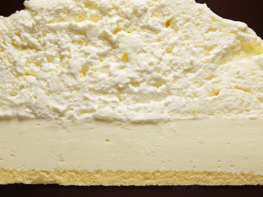 Macro close-up of a dessert with layers of sponge cake, custard, and whipped cream against a dark background.