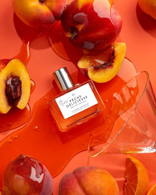 Peach perfume bottle on a red background with fresh peaches, peach slices, and clear viscous liquid creating a visually appealing still life.