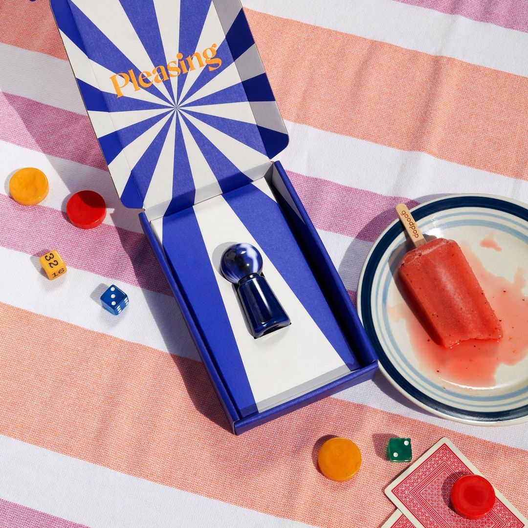 High-angle view of an open blue-striped box with a blue game piece, dice, playing cards, and a popsicle on a striped tablecloth.