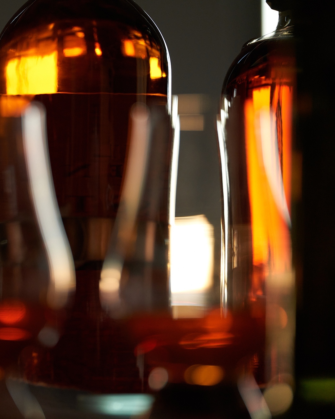 Close-up photo of two amber-colored glass bottles, reflecting warm light, conveying a sense of vintage elegance and craftsmanship.