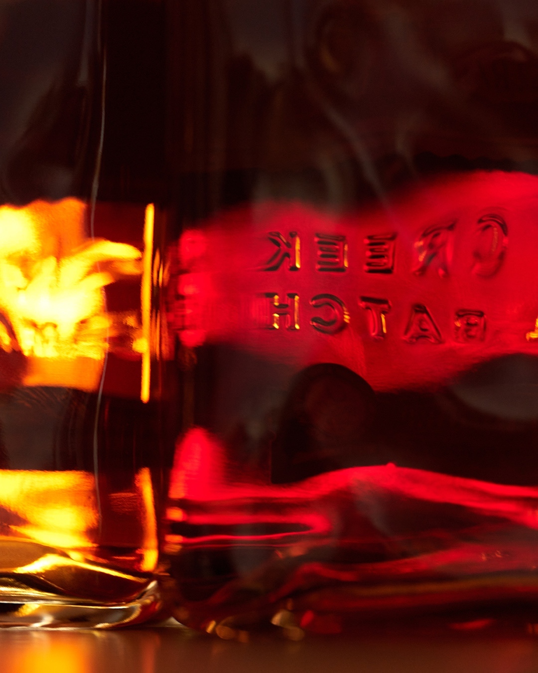 Close-up of a glass bottle filled with amber-colored liquid, featuring raised lettering and glowing edges.