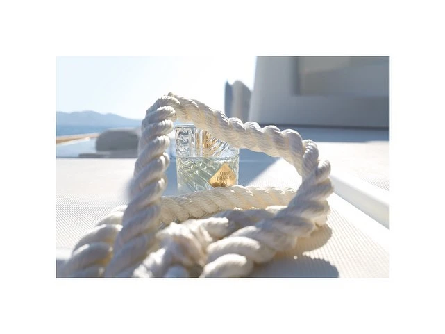 Close-up of a perfume bottle and white rope on a boat deck, capturing a maritime essence under bright natural light with a sea view.