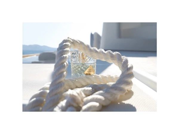 Close-up of a perfume bottle and white rope on a boat deck, capturing a maritime essence under bright natural light with a sea view.