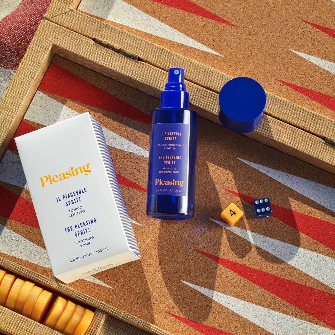 Pleasing skincare product bottle and container with dice and game pieces on a patterned surface with hues of brown, white, and red.