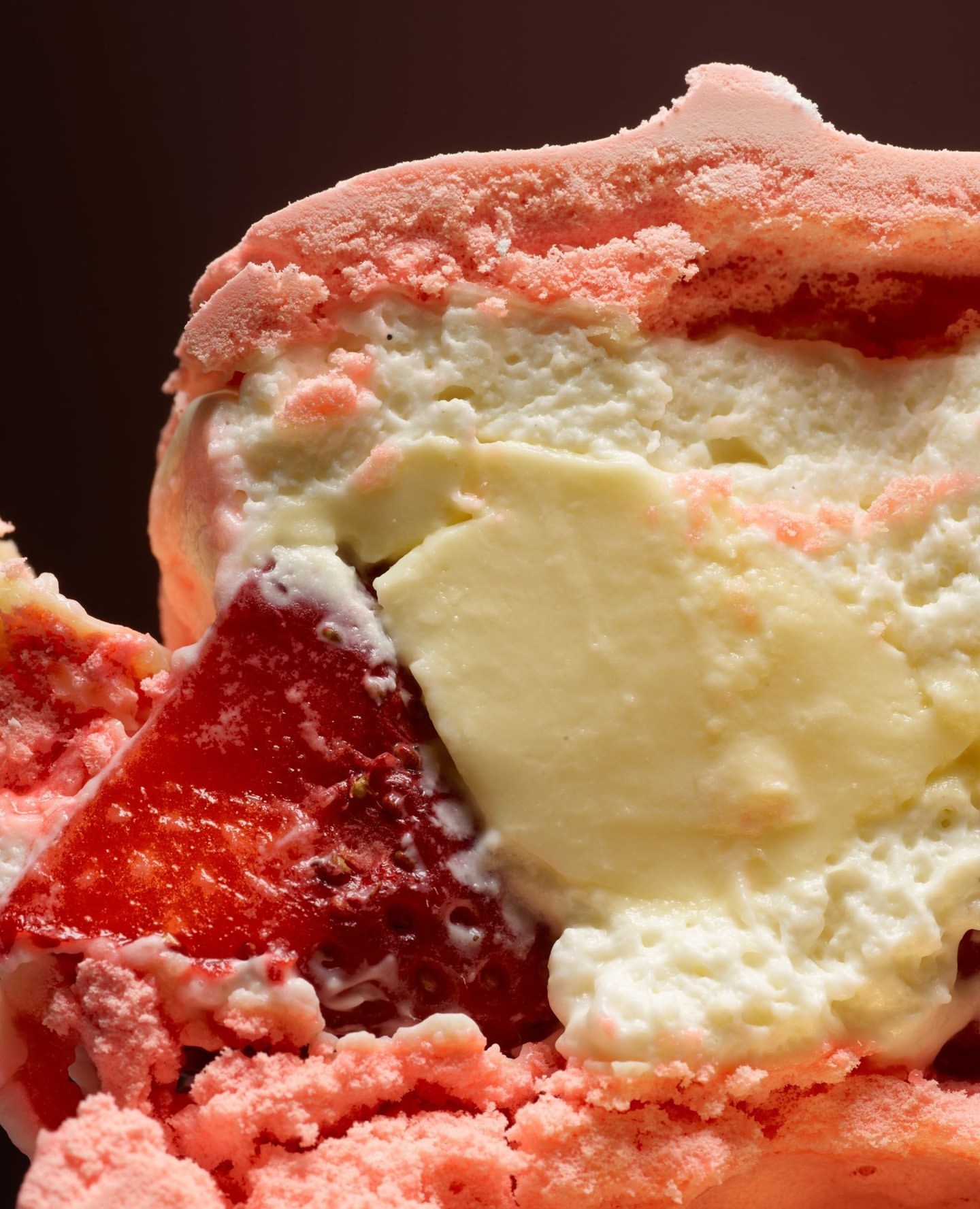 Close-up of a sweet dessert featuring layers of cream, strawberry gelatin, and pink sponge cake, showcasing its textures and colors.
