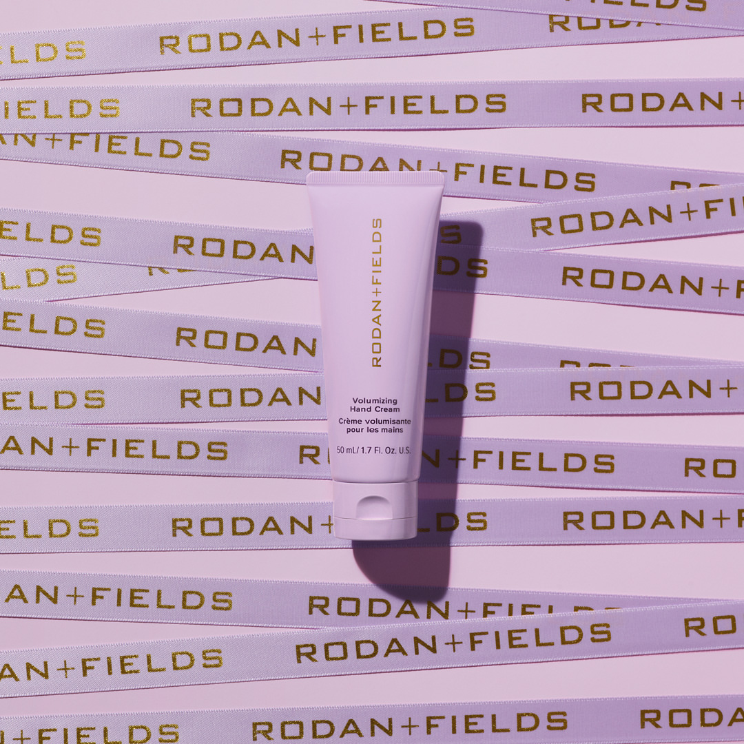 Rodan + Fields Volumizing Hand Cream tube centered among branded ribbons in a flat lay studio shot.