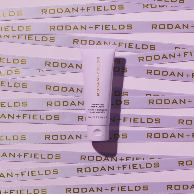 Rodan + Fields Volumizing Hand Cream tube centered among branded ribbons in a flat lay studio shot.