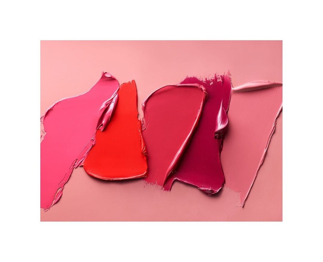 Cosmetic beauty product shot of smears of lipstick in a range of pink and red tones, against a pink background. Beauty product photography.