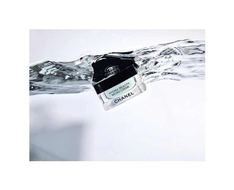 Beauty shot of Chanel Hydra Beauty Micro Crème jar with black lid partly submerged in clear water creating surface tension ripples.