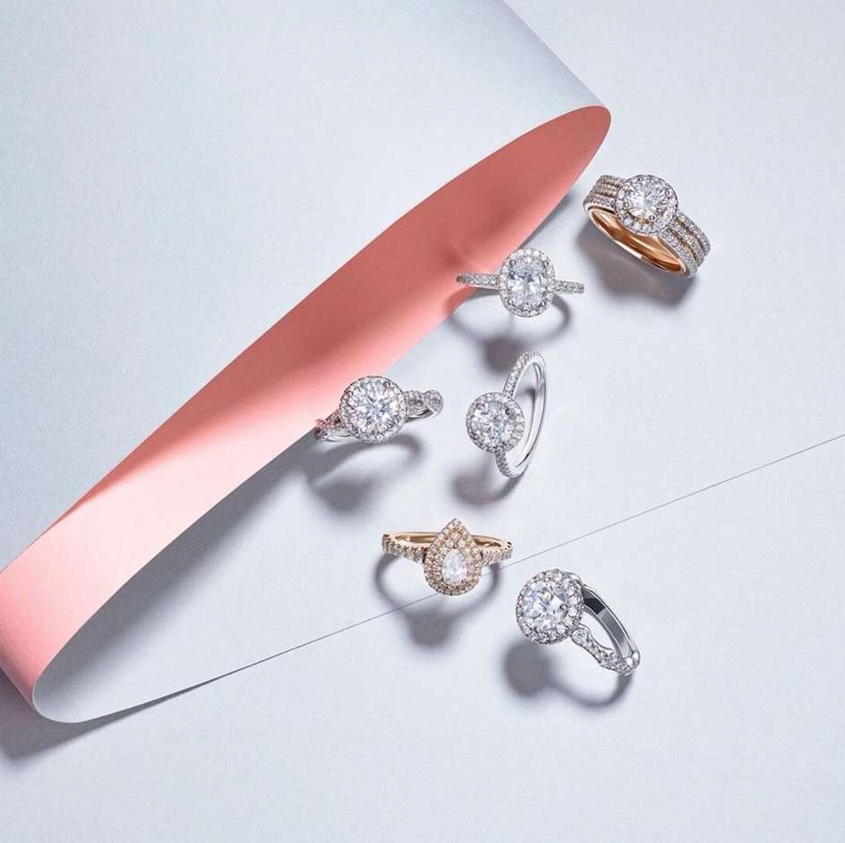 Multiple diamond rings displayed on a white surface with a soft pink ribbon, showcasing jewelry and elegant design elements for advertising.