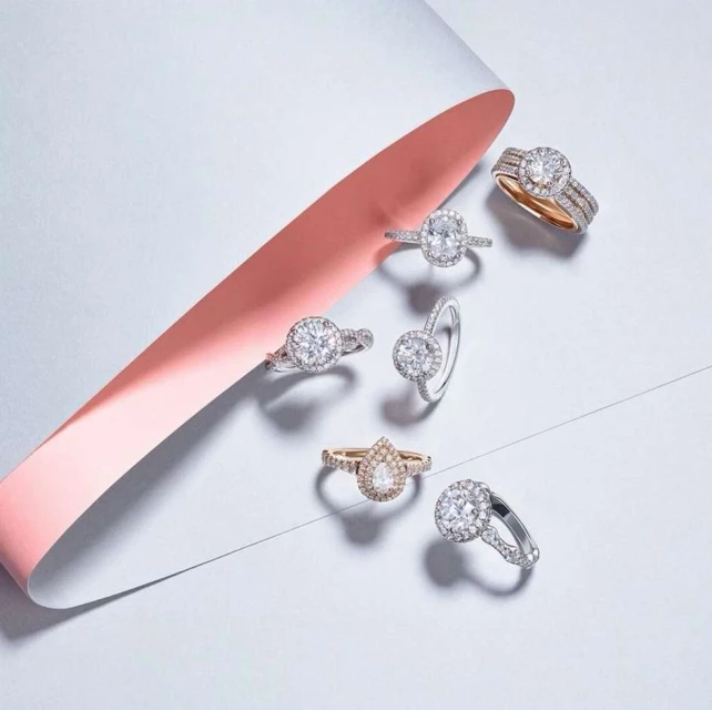 Multiple diamond rings displayed on a white surface with a soft pink ribbon, showcasing jewelry and elegant design elements for advertising.