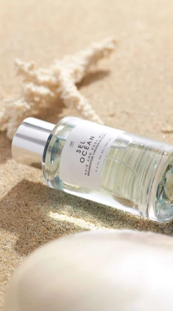 Close-up of hair and body mist bottle on sand with sea star, evoking a summery, beachy aesthetic for beauty and lifestyle promotions.