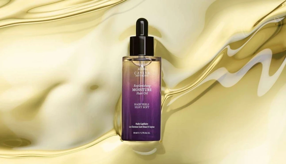 Close-up studio shot of a bottle of Caviar Anti-Aging Replenishing Moisture Hair Oil against a golden liquid background.