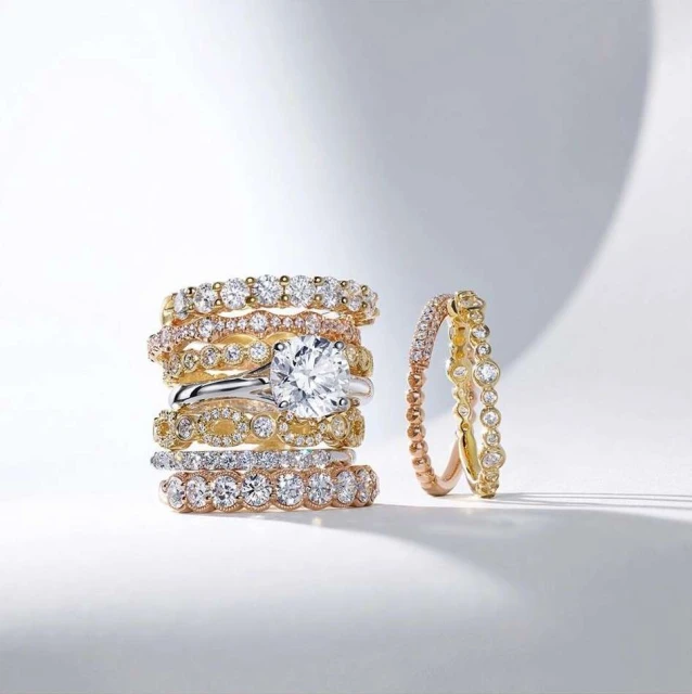 A stack of multiple gold and diamond rings, featuring a solitaire diamond ring, in a product shot against a gradated white background.