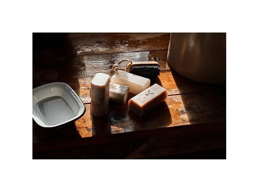 Still life featuring bar soaps, dish, and scrub brush on wood surface. Rustic bathroom or spa scene with organic cleansing items.