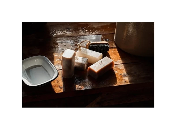 Still life featuring bar soaps, dish, and scrub brush on wood surface. Rustic bathroom or spa scene with organic cleansing items.