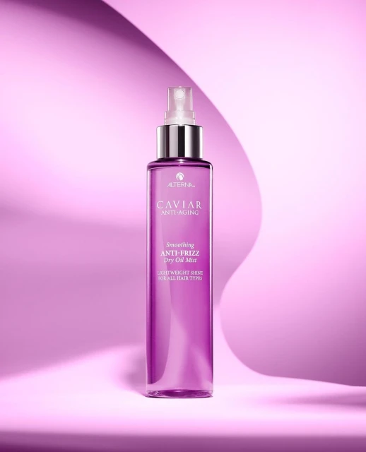 Purple bottle of Alterna Caviar Anti-Aging Smoothing Anti-Frizz Dry Oil Mist against a wavy violet background in a product shot.
