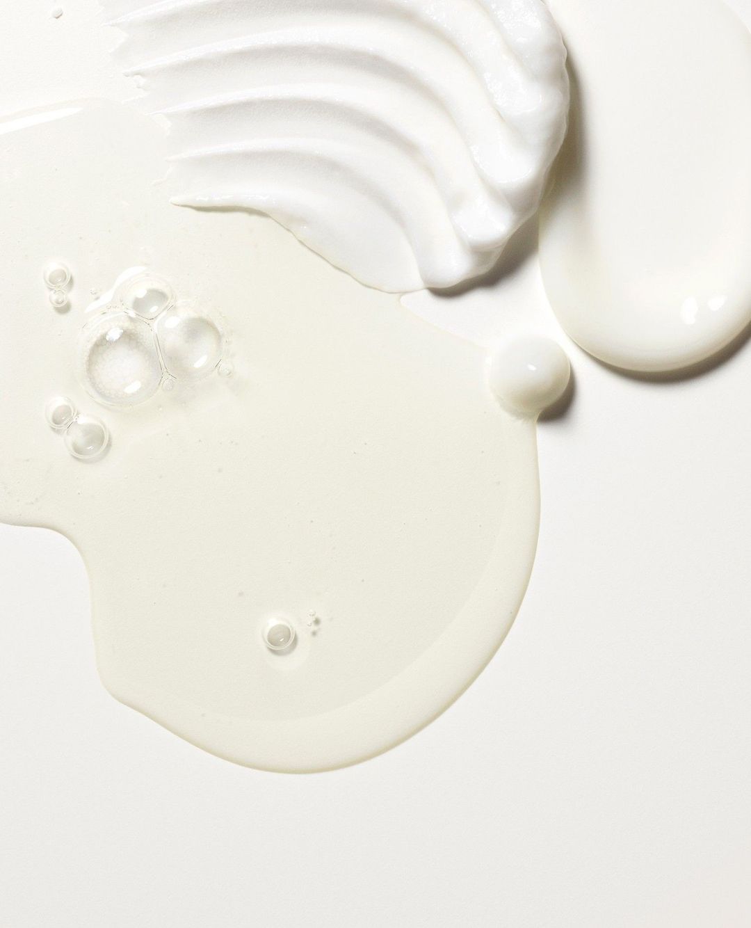 Close-up of three distinct textured white creams and gel, including transparent bubbles, against a white background in vertical format.