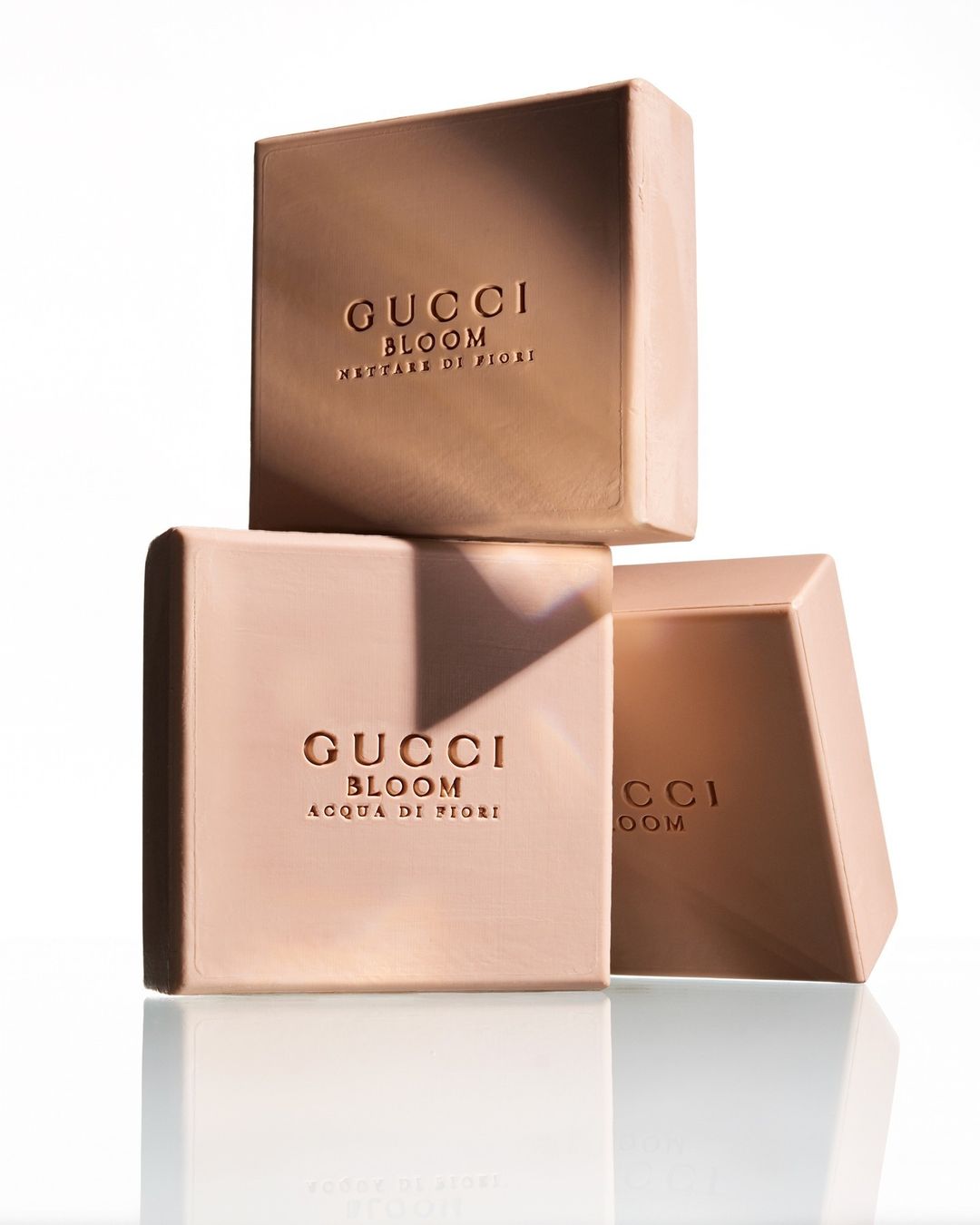 Stacked Gucci Bloom perfume boxes on a reflective surface, presenting a minimalist beauty product shot with neutral color tones.