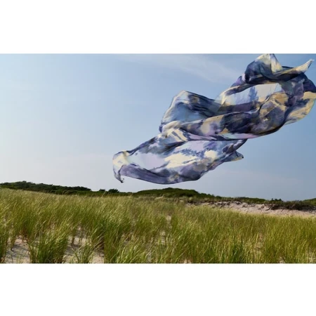 A fabric floats in the air over tall green grass growing on sand dunes underneath a blue sky. Landscape orientation, sunny day.