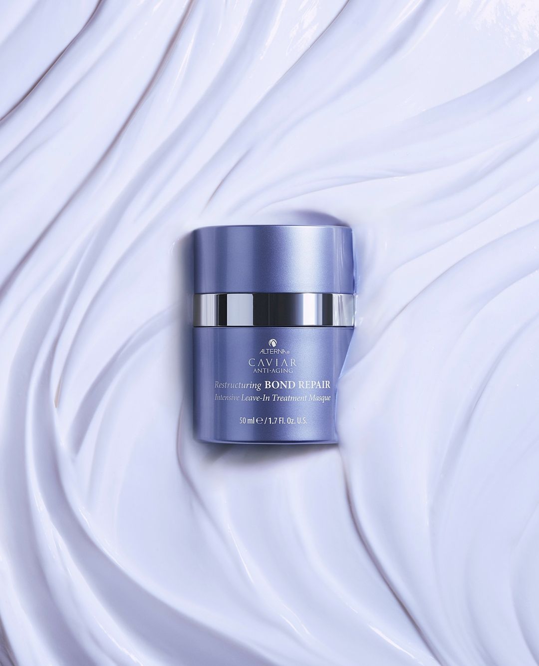 A purple and silver container of Alterna Caviar Bond Repair Masque is centered on a backdrop of textured, light-purple creme.
