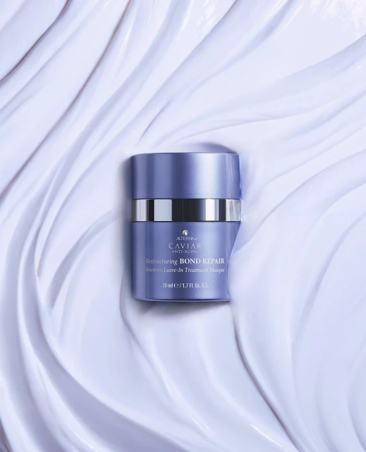 A purple and silver container of Alterna Caviar Bond Repair Masque is centered on a backdrop of textured, light-purple creme.