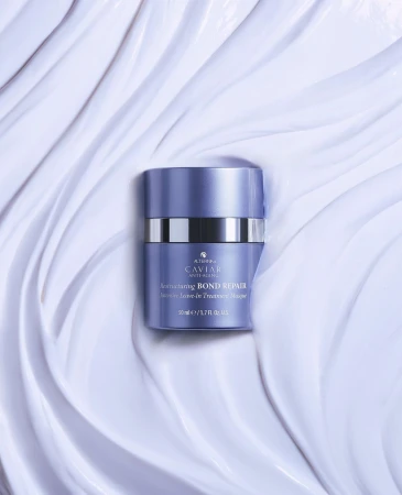 A purple and silver container of Alterna Caviar Bond Repair Masque is centered on a backdrop of textured, light-purple creme.