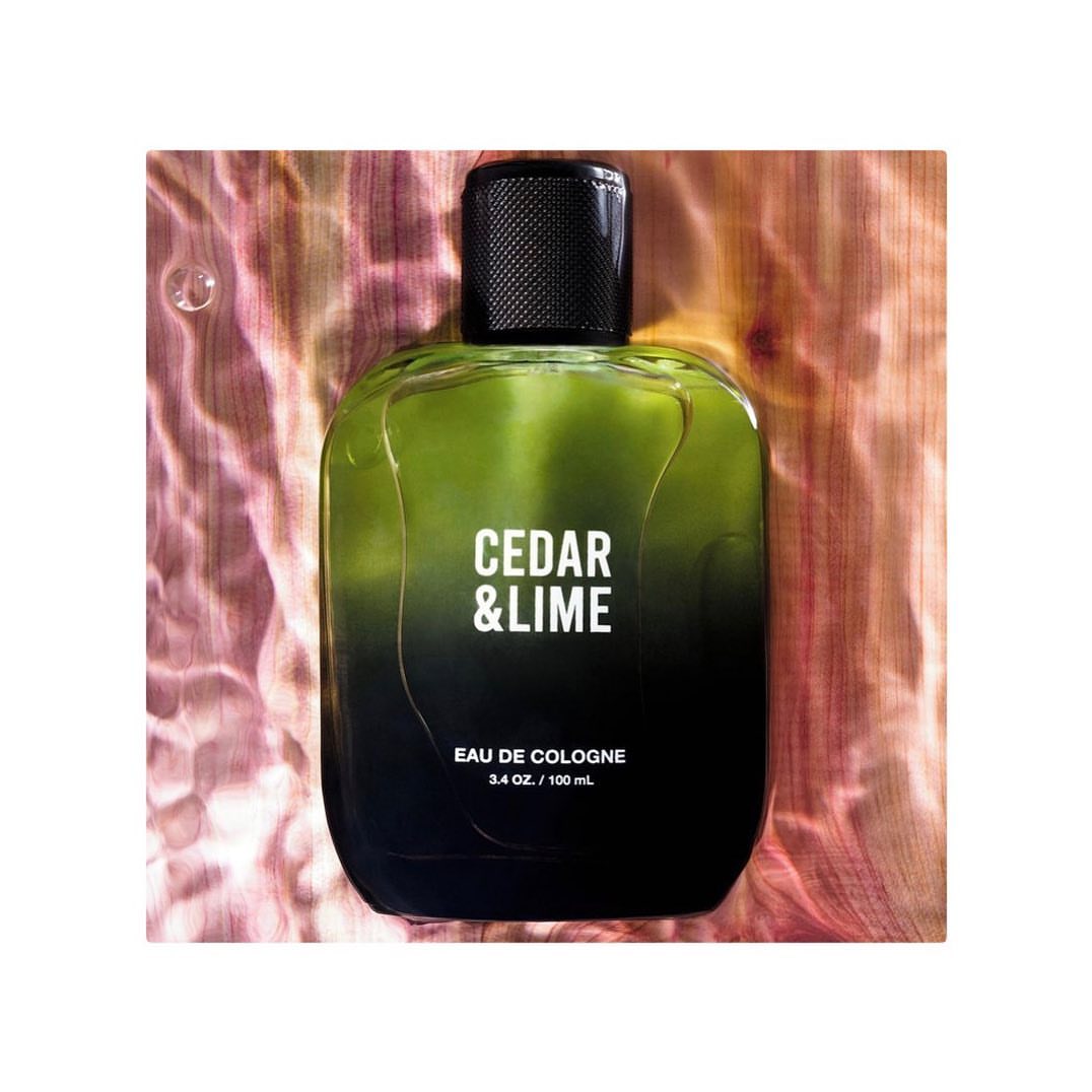 A bottle of Cedar & Lime eau de cologne with black cap on a water-like surface with pink and green tones in a studio setting.