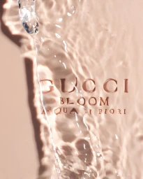 Crystal clear water splashing over a smooth pale pink surface with embossed Gucci Bloom typography.