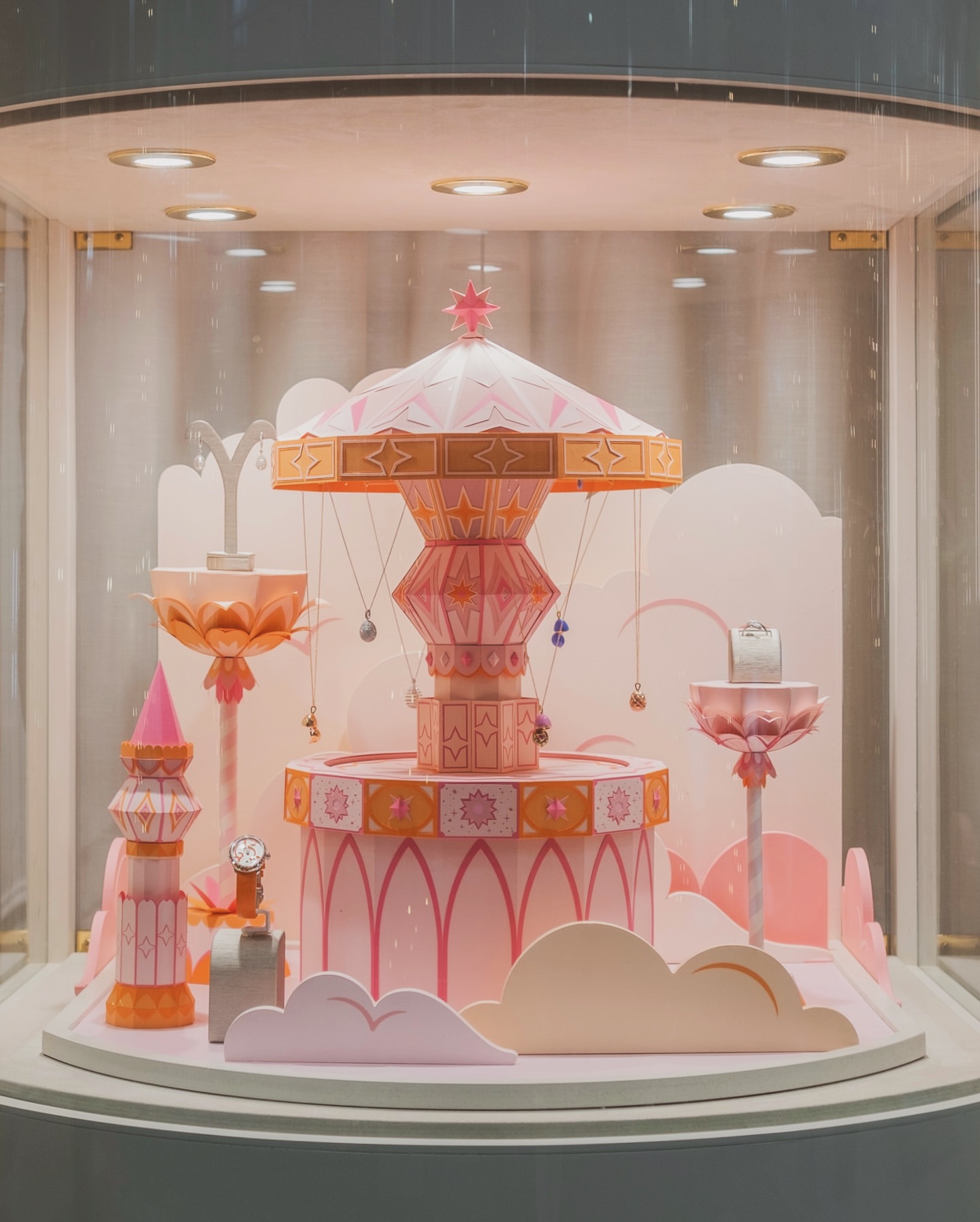 Carousel jewelry display in a store window, featuring necklaces, earrings, watches and rings in a pink and orange color scheme.