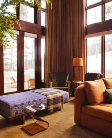 Interior view of a living room with an orange sofa, purple patterned daybed, and large windows looking out onto a snowy landscape.