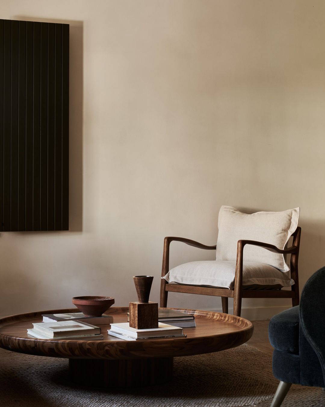 Living room interior with wooden coffee table, armchair, decor objects, wall art, and neutral tones, creating a cozy and modern atmosphere.
