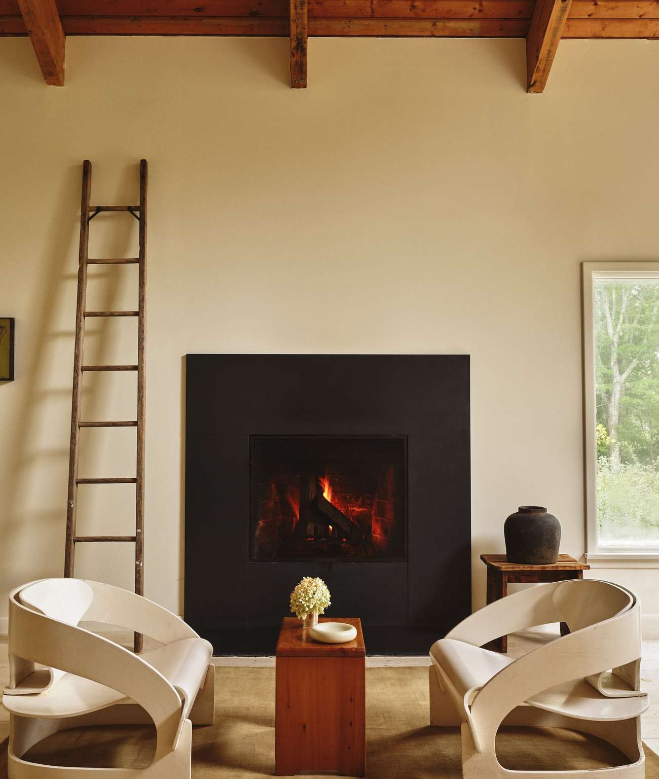 Interior of a living room featuring a fireplace with a black frame, two armchairs, a ladder, and a wooden coffee table.