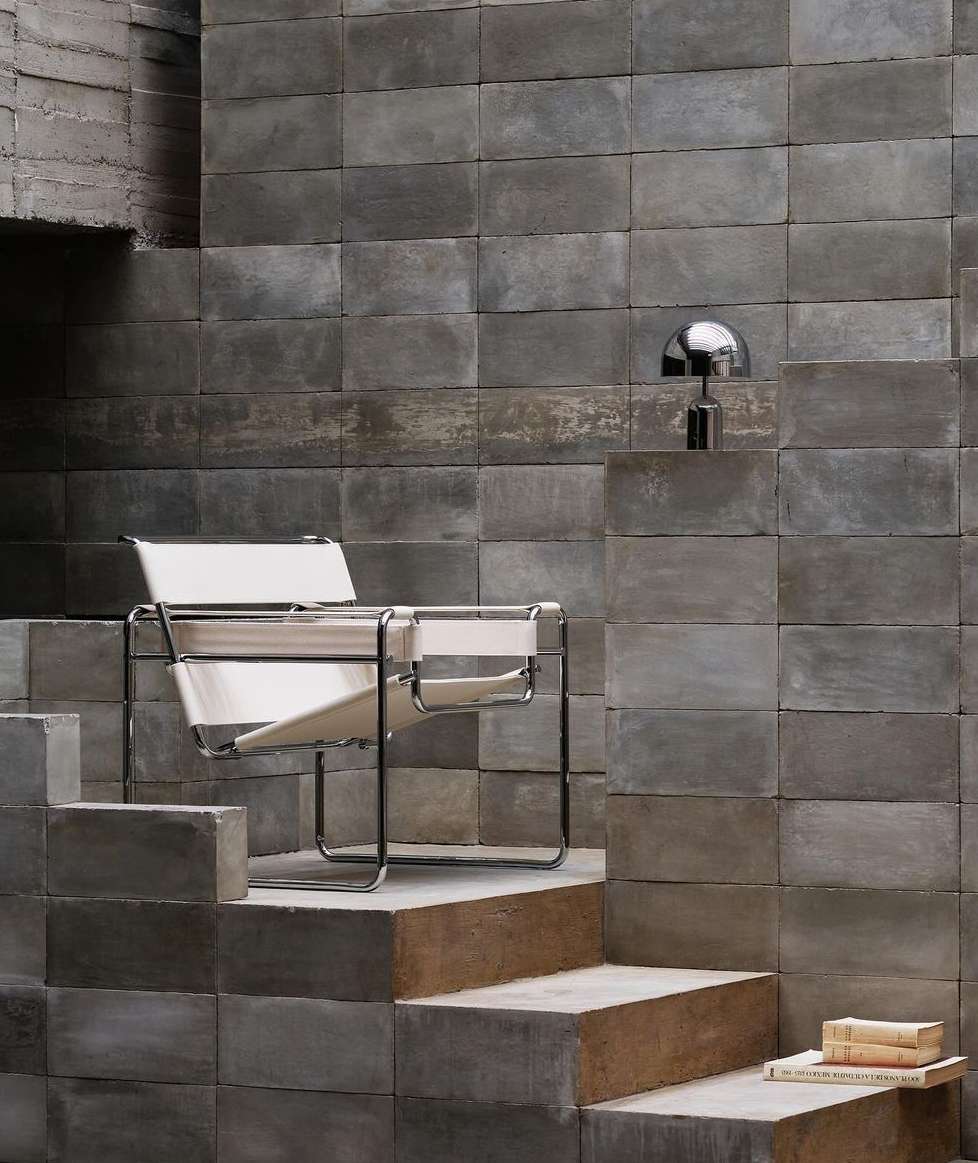 Modern architectural interior with a black chrome chair with white straps, a chrome mushroom lamp, and concrete blocks in gray tones.