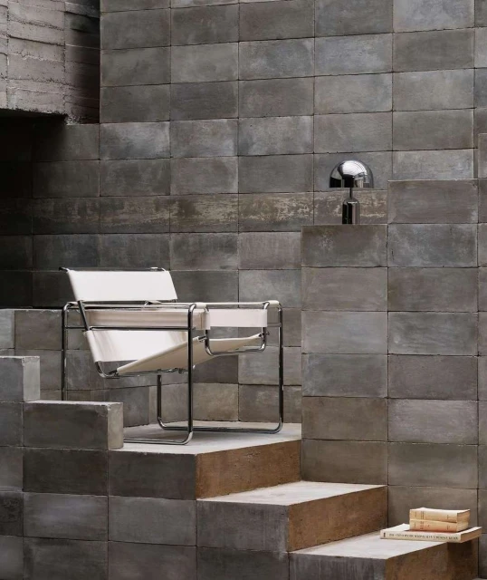 Modern architectural interior with a black chrome chair with white straps, a chrome mushroom lamp, and concrete blocks in gray tones.