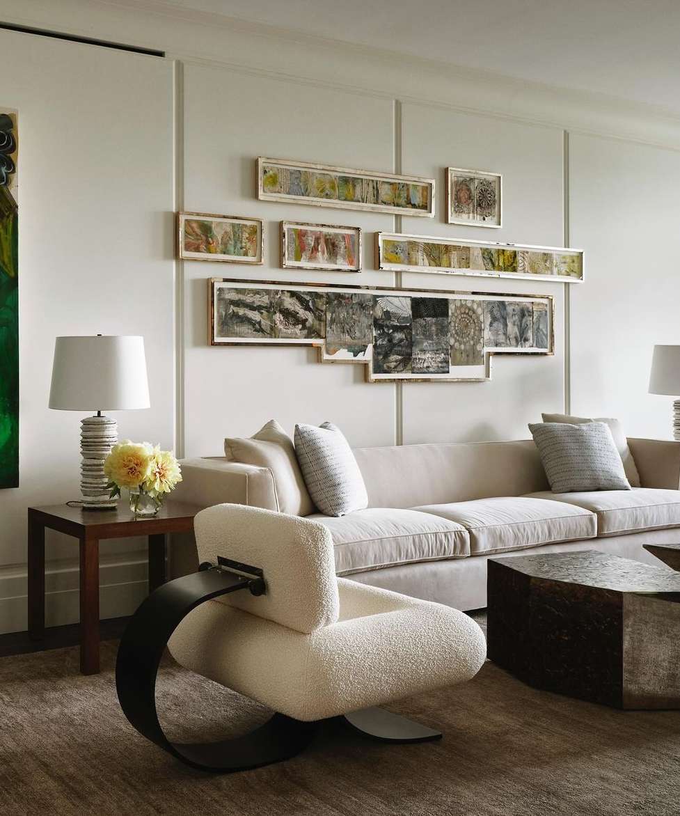 Living room interior featuring a modern armchair, neutral sofa with pillows, a wood coffee table, and artwork on the light-colored wall.