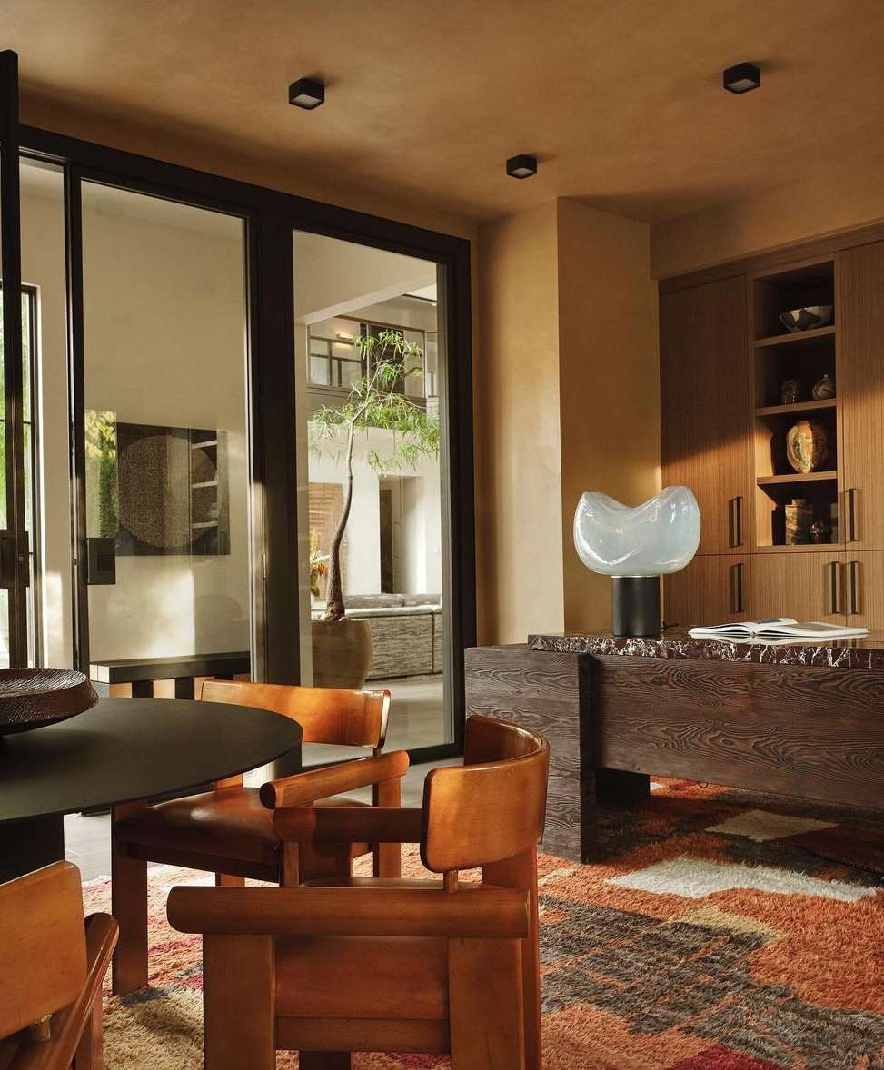 Interior view of a modern dining room with wood chairs, table, decorative lamp, and a view to an outdoor space through sliding glass doors.
