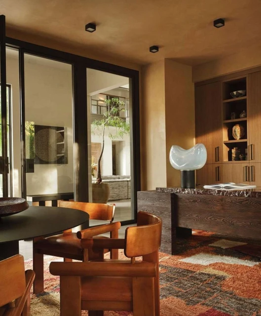 Interior view of a modern dining room with wood chairs, table, decorative lamp, and a view to an outdoor space through sliding glass doors.