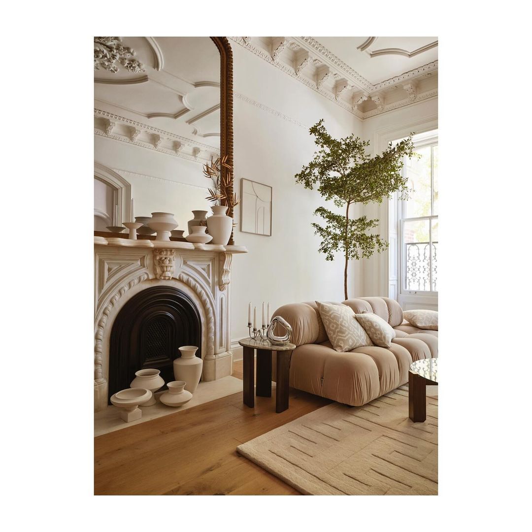 Living room interior with a beige modular sofa, coffee tables, and decorative fireplace with vases in a stylish, neutral-toned space.