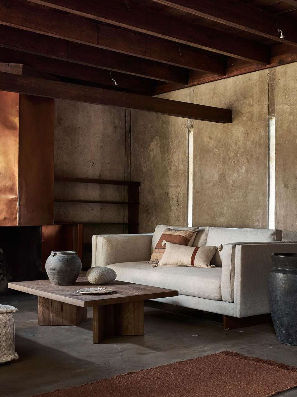 Living room with a neutral couch, wooden coffee table topped with decorative items, and large decorative jars against a concrete wall.