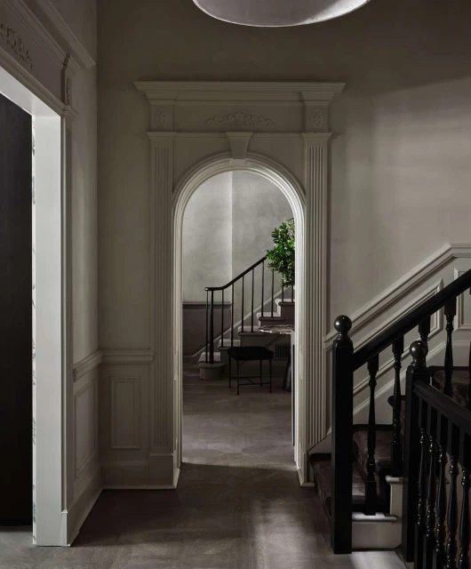 Interior view showcases an arched doorway leading to stairs with black railings and an adjacent doorway in a room with neutral tones.