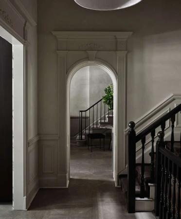 Interior view showcases an arched doorway leading to stairs with black railings and an adjacent doorway in a room with neutral tones.