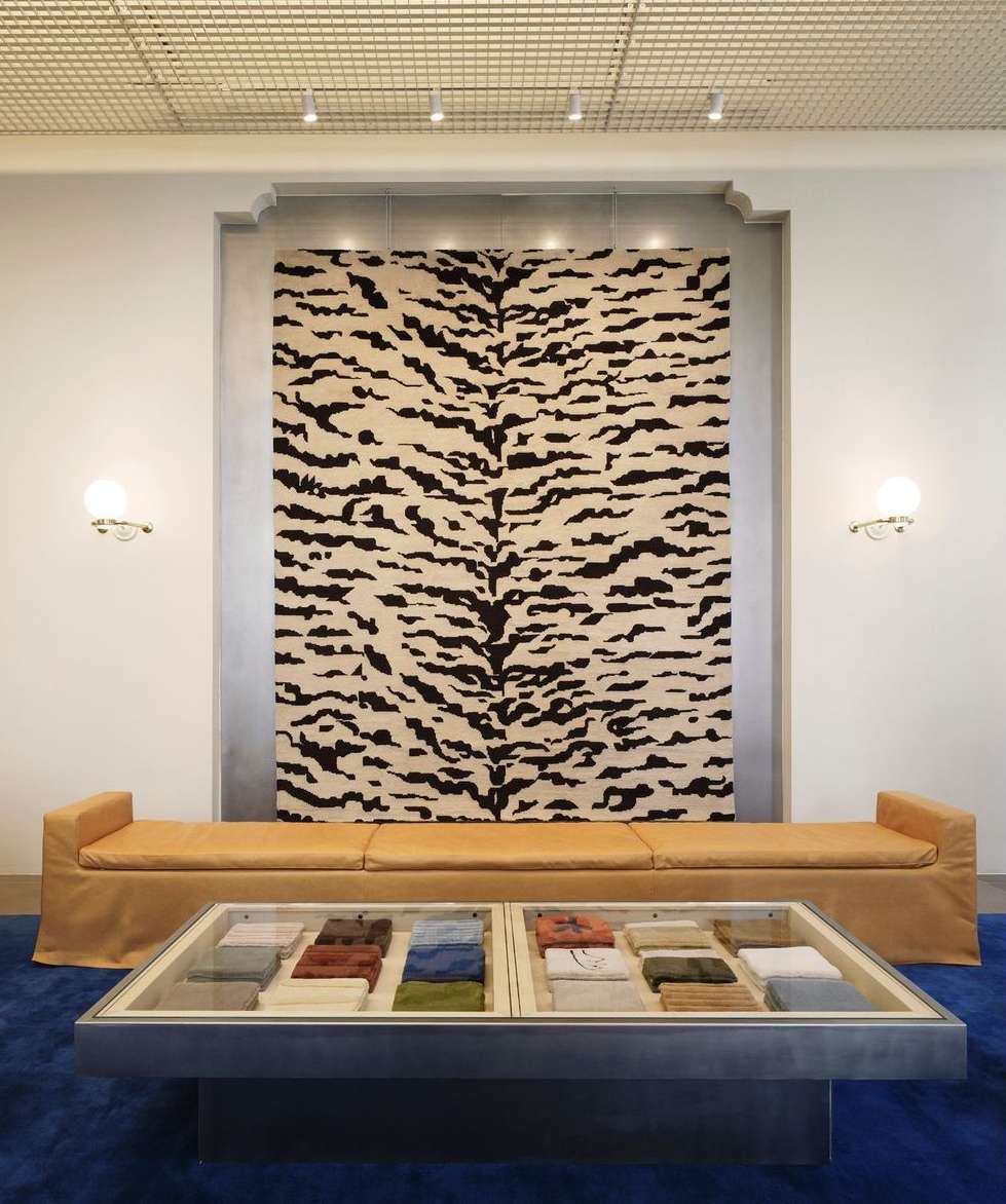 Interior design featuring a tiger-striped rug hanging on the wall, a sofa, and a coffee table with fabric samples in a showroom setting.